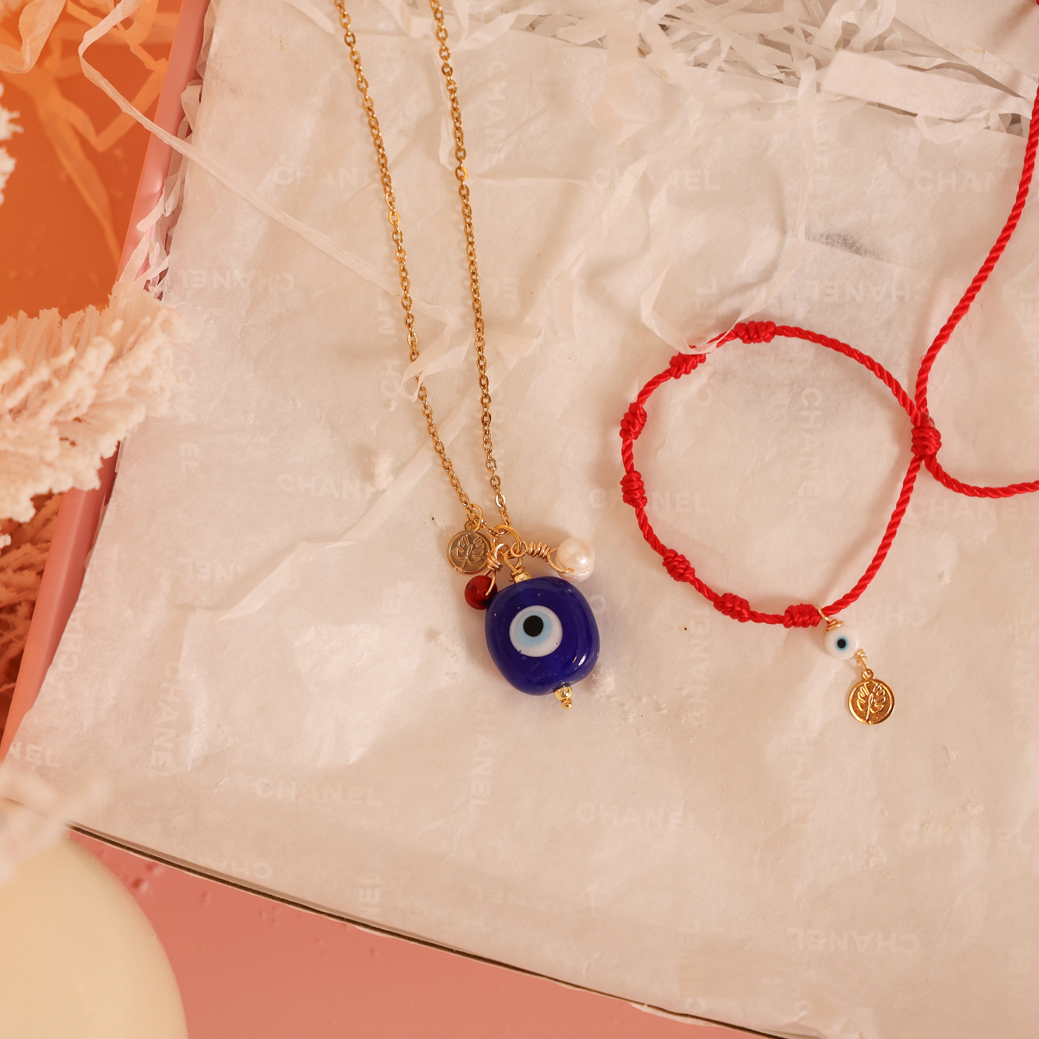 Necklace with a blue evil eye pendant and red bracelet on a textured surface.