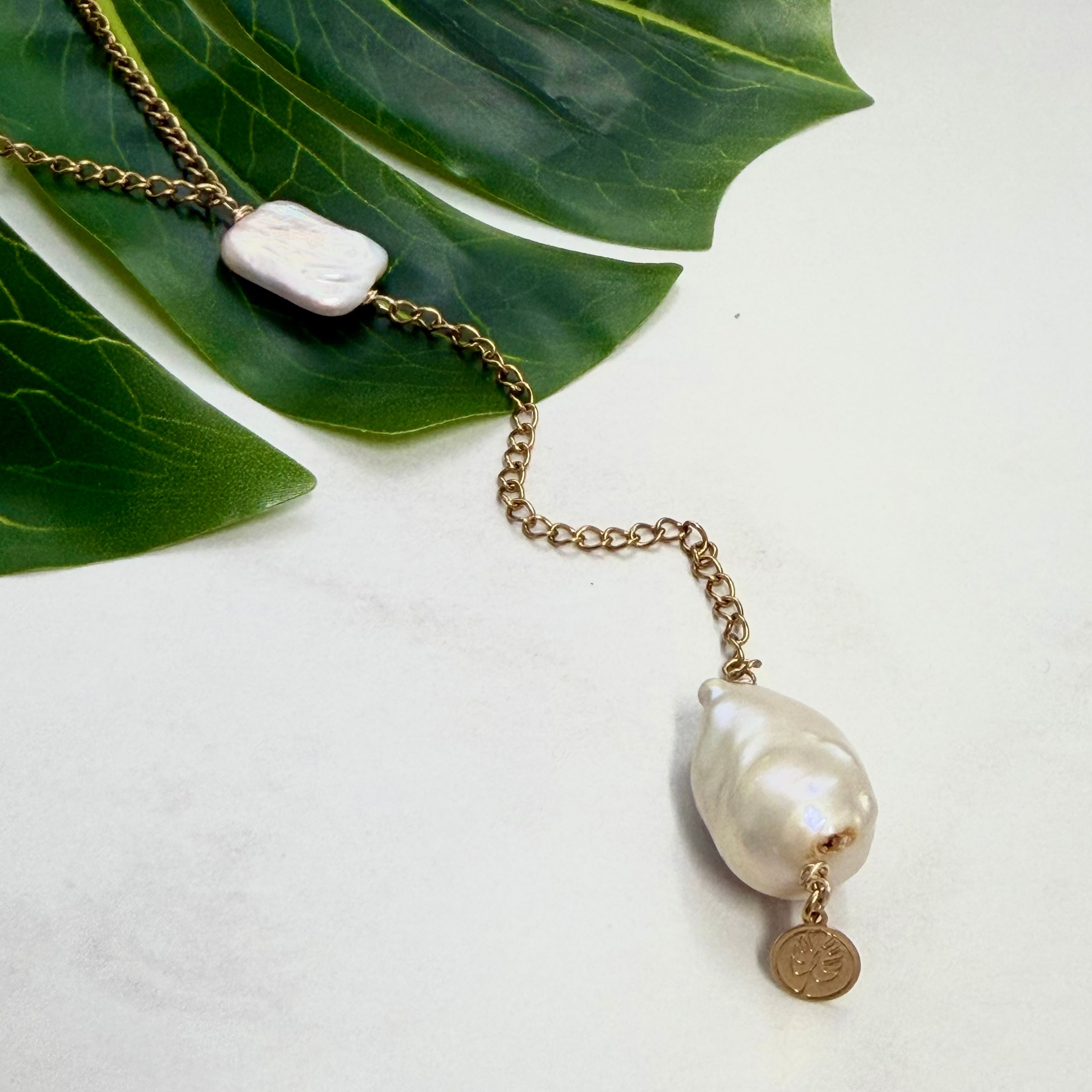 Necklace with pearls and a gold chain on a white background with green leaves.